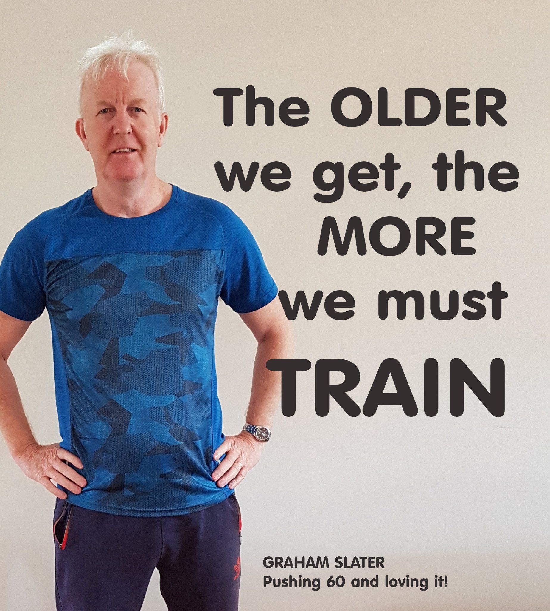 A man is standing with his hands on his hips in front of a wall that says the older we get the more we must train