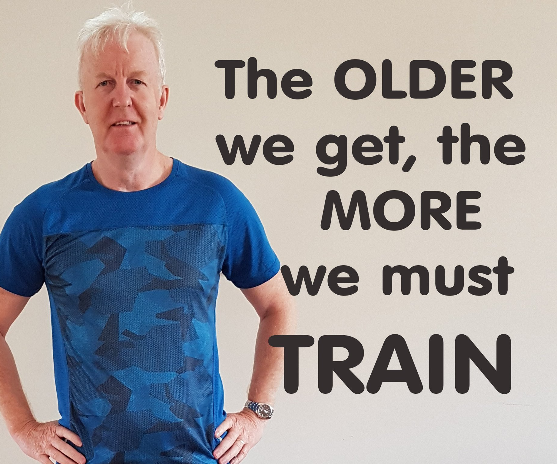 A man in a blue shirt is standing in front of a sign that says the older we get the more we must train