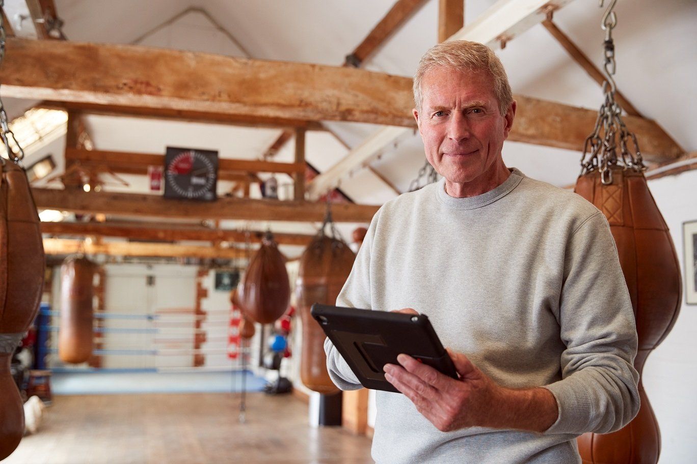 A man is holding a tablet in a boxing gym.
