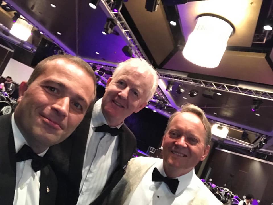 Three men in tuxedos and bow ties are posing for a picture