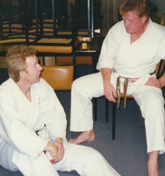 Two men in white karate uniforms are sitting on the floor talking