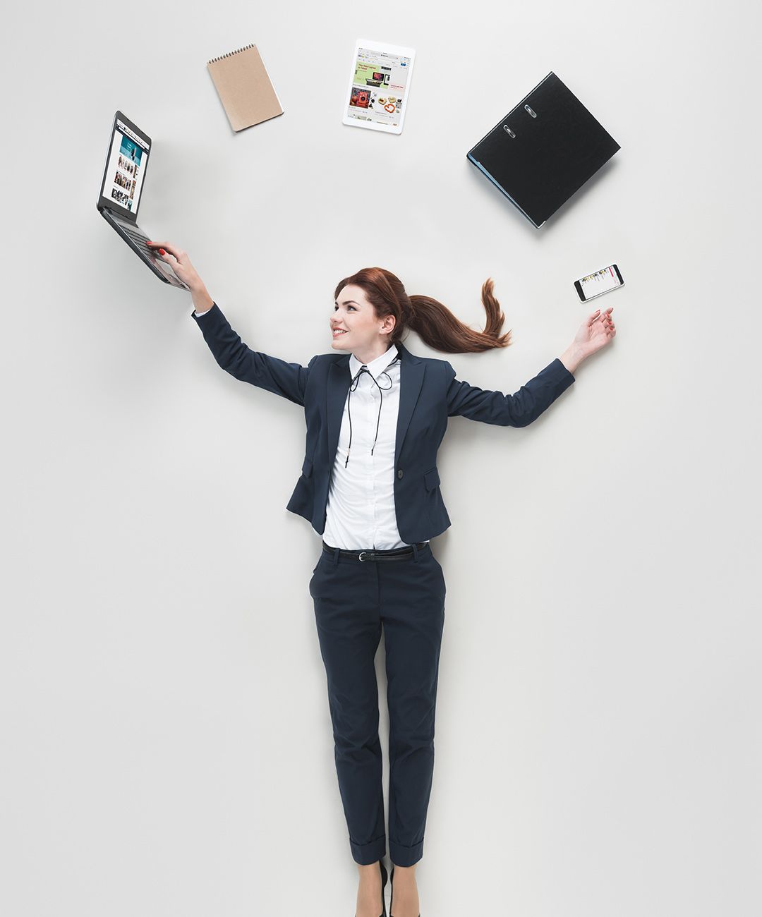 A woman in a suit is laying on the floor holding a laptop