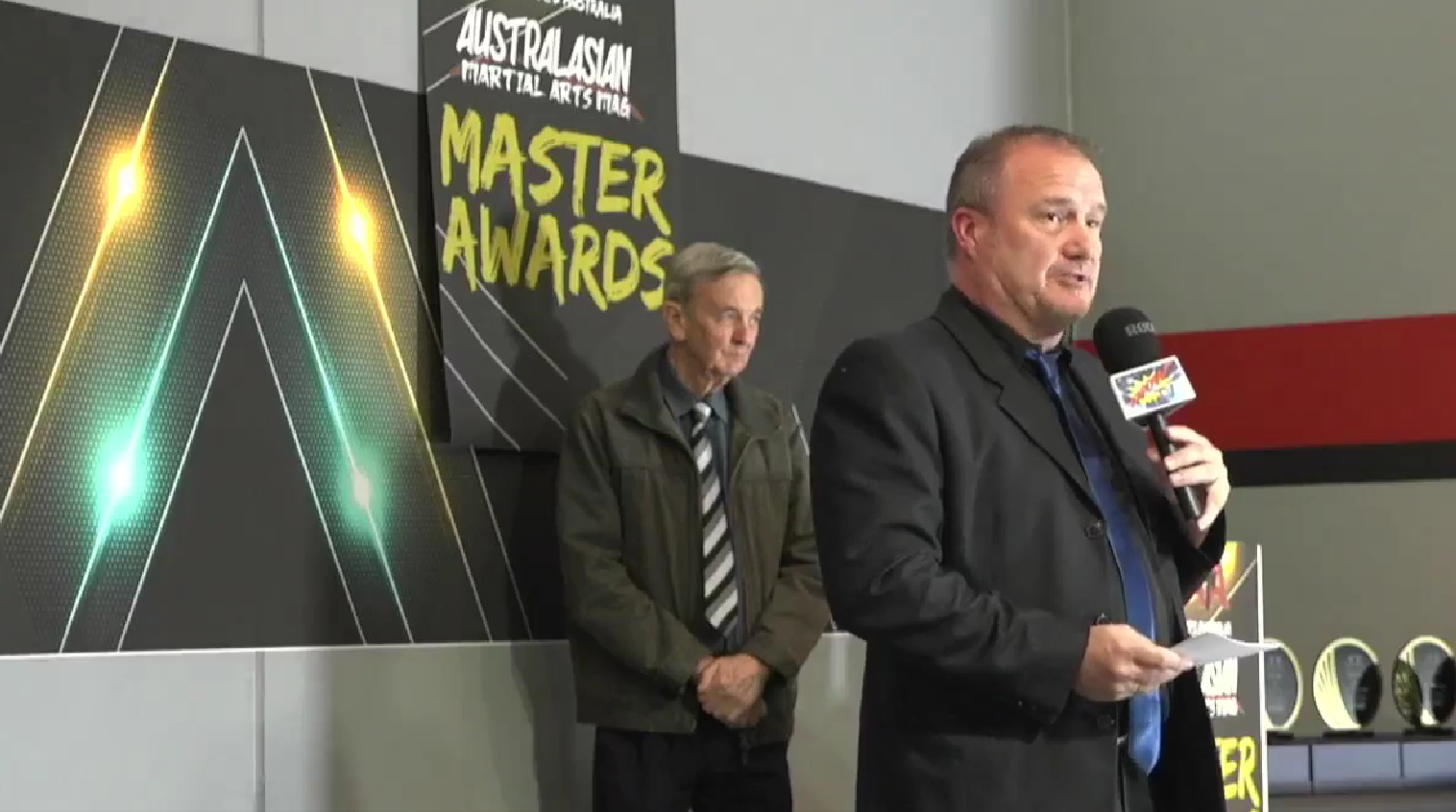 Two men are standing in front of a sign that says master awards