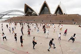 A large group of people are dancing in front of the opera house in sydney.