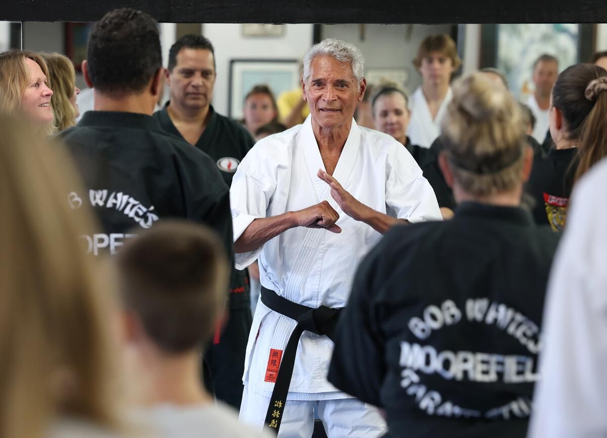 Karate instructor in white gi with black belt, demonstrating technique to group of students.