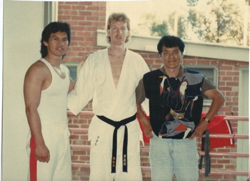 Three men posing for a picture with one wearing a black belt