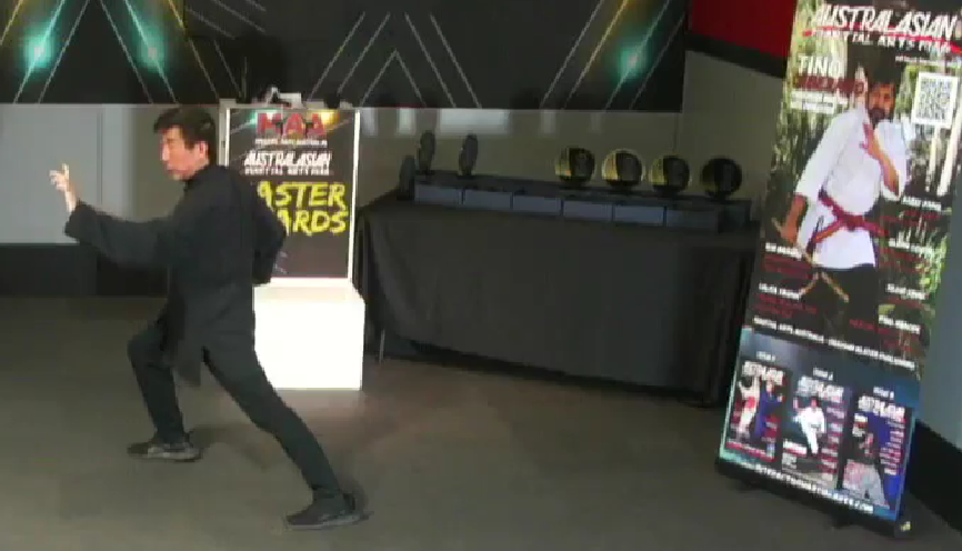 A man is practicing martial arts in front of a sign that says master awards