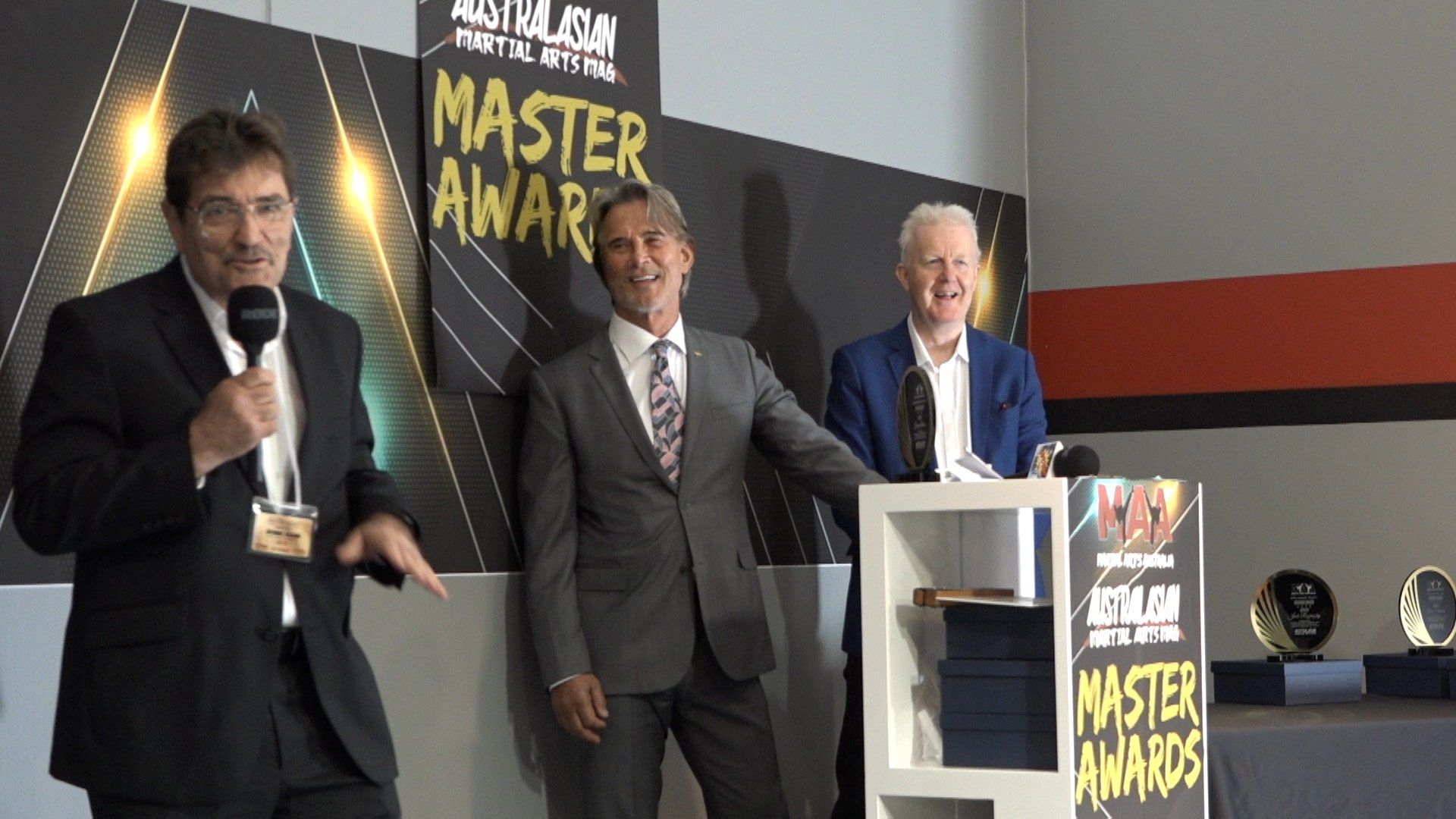Three men in suits are standing in front of a sign that says master awards