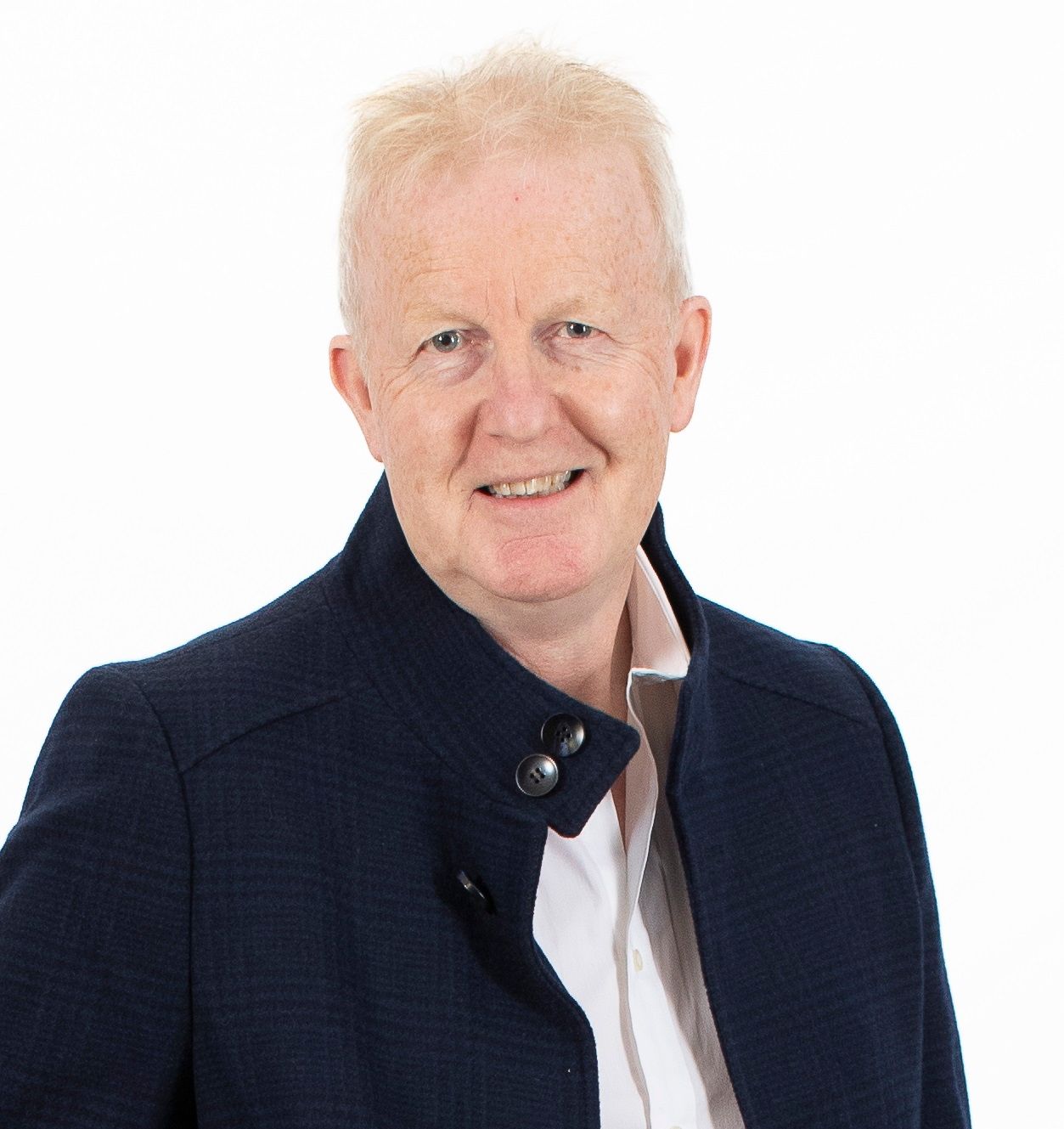 A man wearing a blue jacket and a white shirt is smiling for the camera.