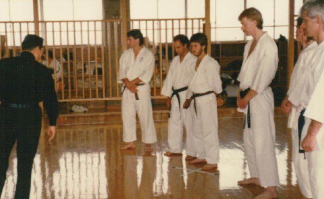 A group of men in karate uniforms are standing on a wooden floor.