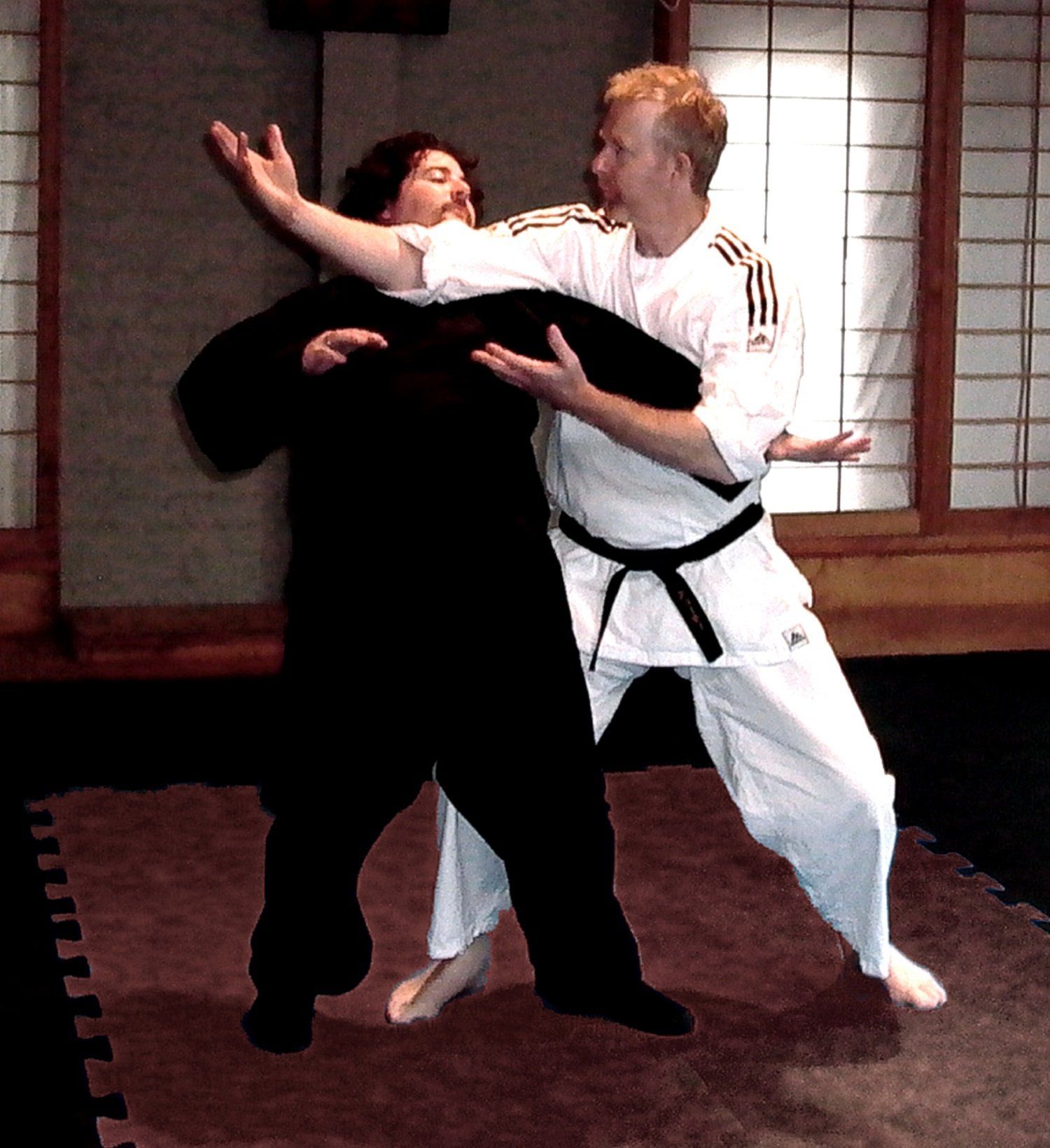 A man in a karate uniform is holding another man in a black belt