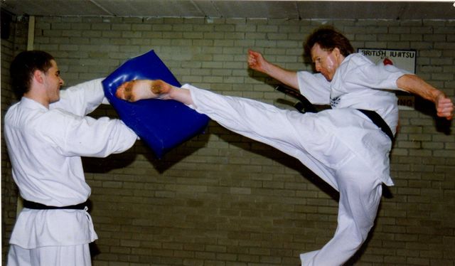 A man kicking a blue pad while another man watches