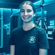 A woman in a black t-shirt is smiling in a gym.