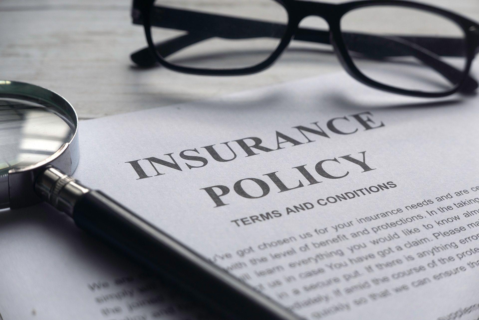 A close up of an insurance policy with glasses and a magnifying glass.