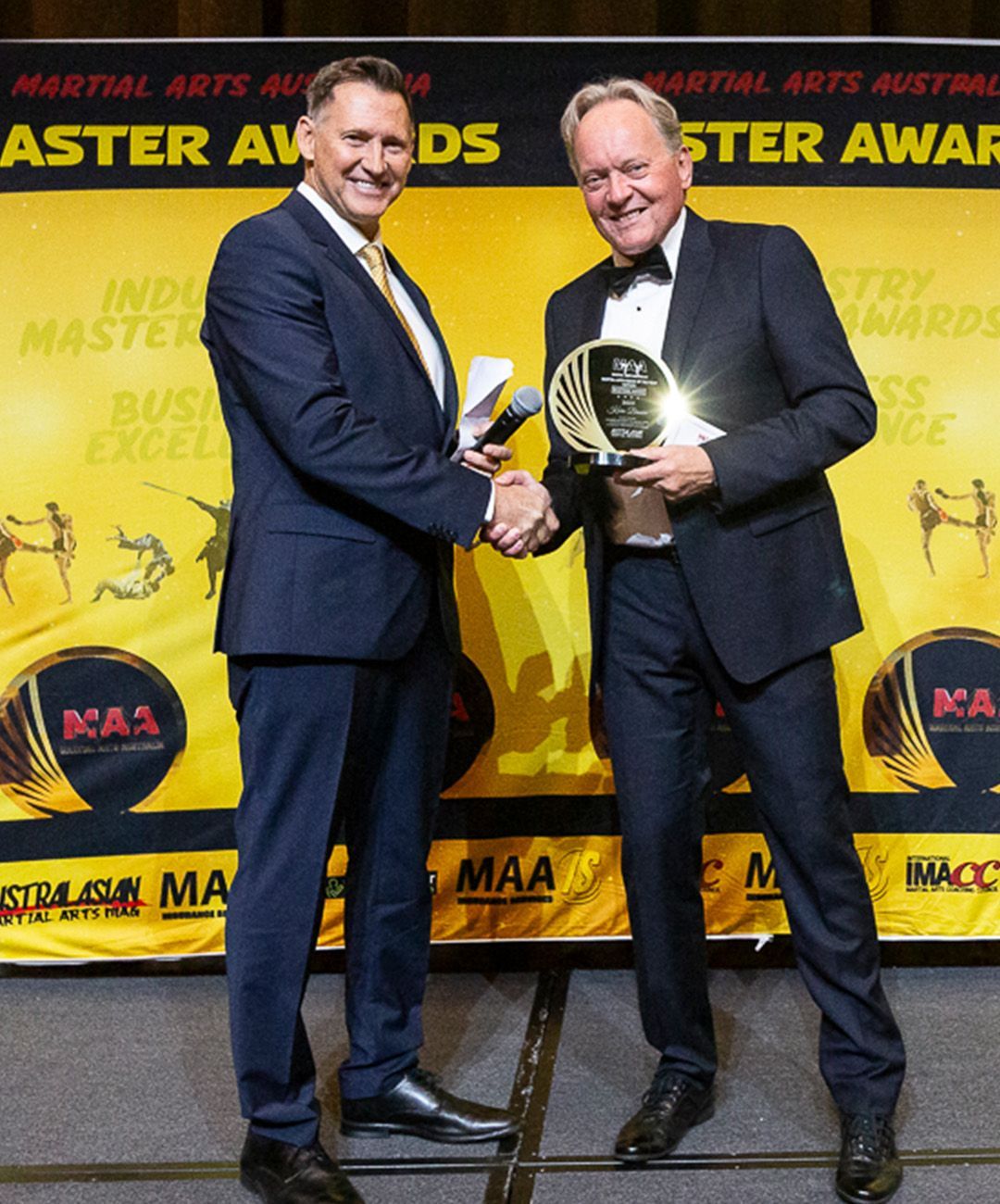 Two men shaking hands in front of a banner that says master awards