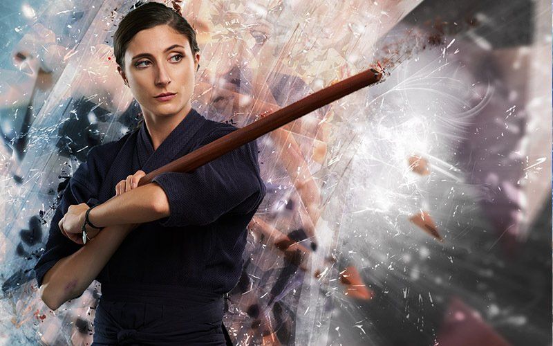 A woman in a karate uniform is holding a wooden stick.