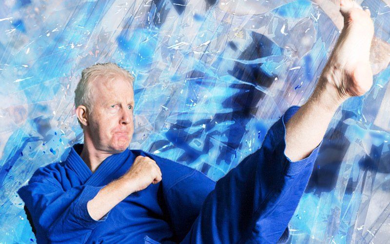 A man in a blue karate uniform is kicking in the air.