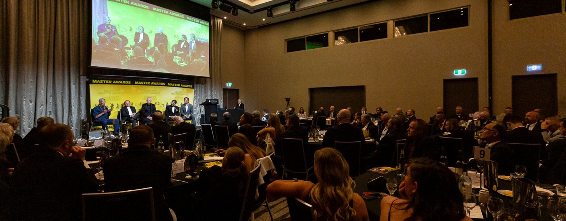 A large group of people are sitting in a large room watching a presentation.