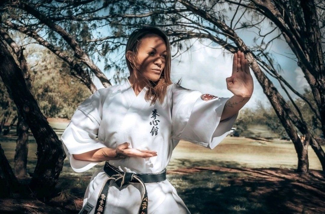 A woman in a karate uniform is practicing karate in the woods.