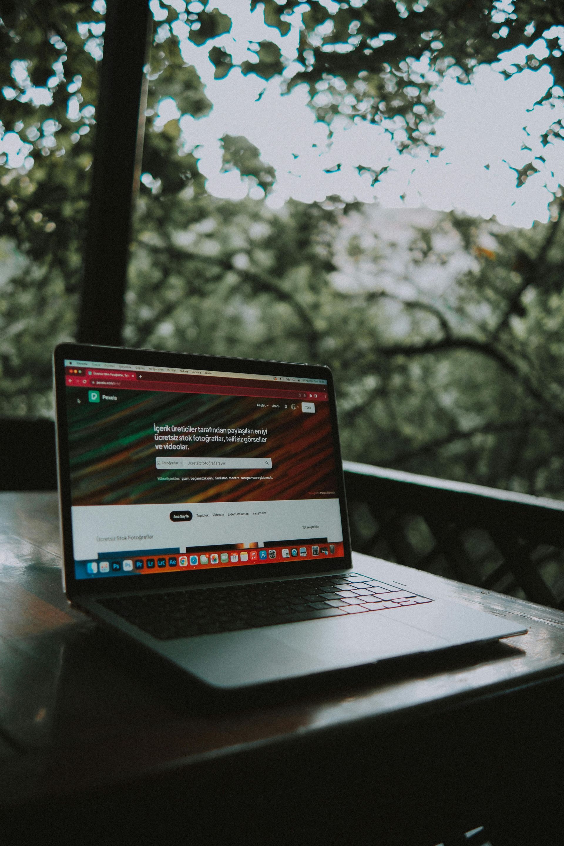 Laptop on a table outdoors, displaying a website with trees blurred in the background.