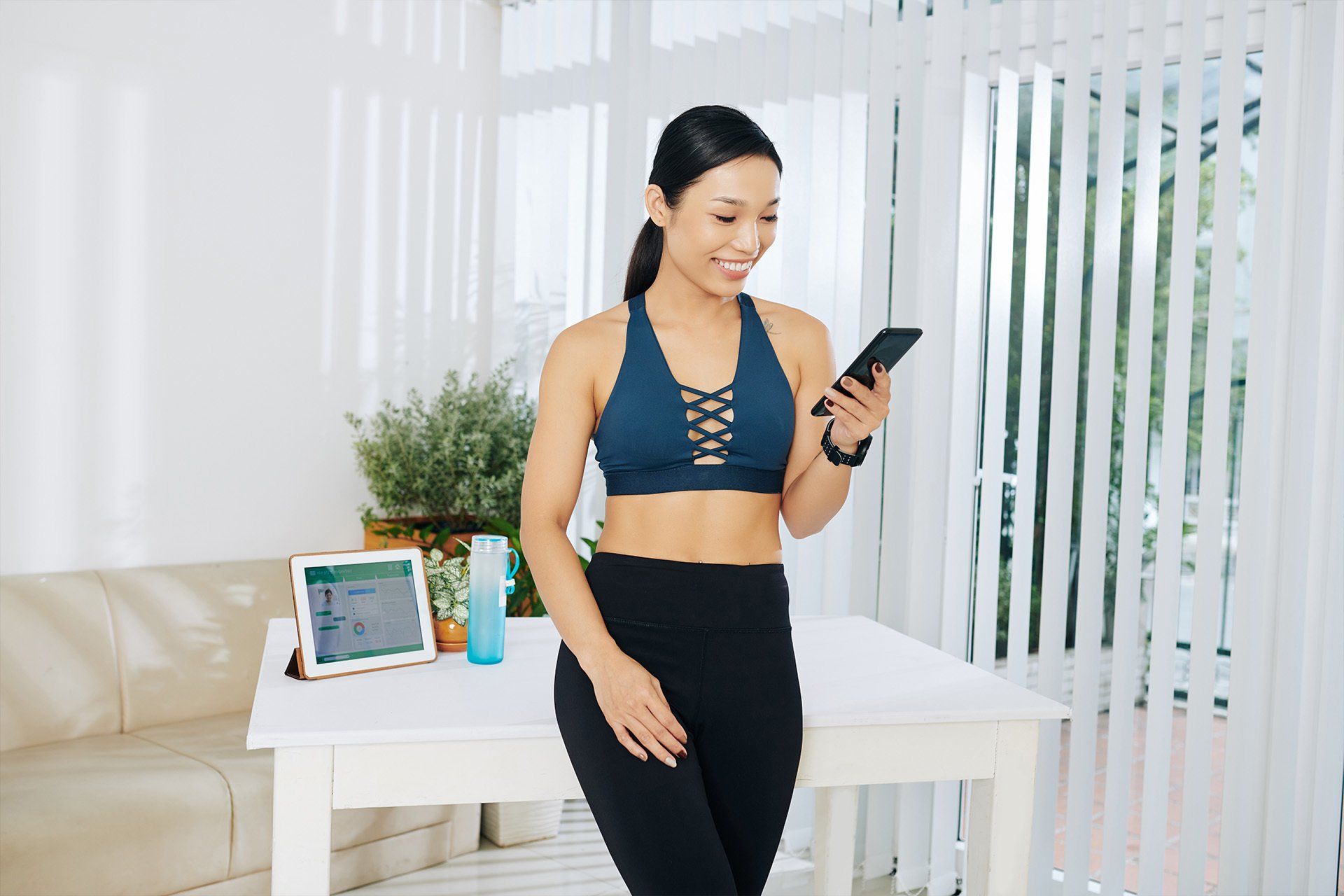 A woman is standing next to a table looking at her cell phone.