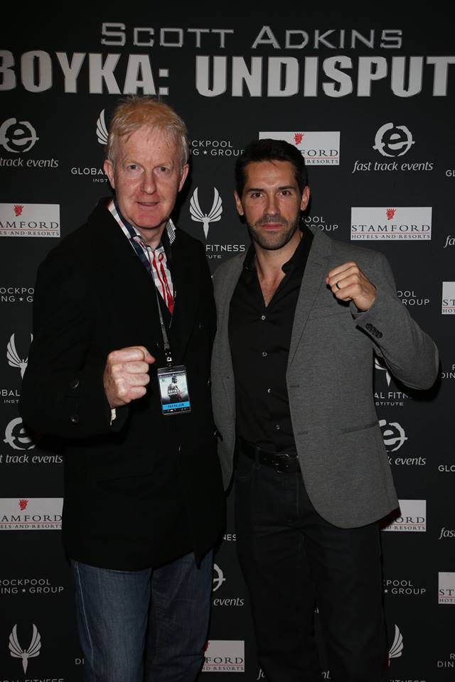 Two men are posing for a picture in front of a wall that says scott adkins boyka: undisputed