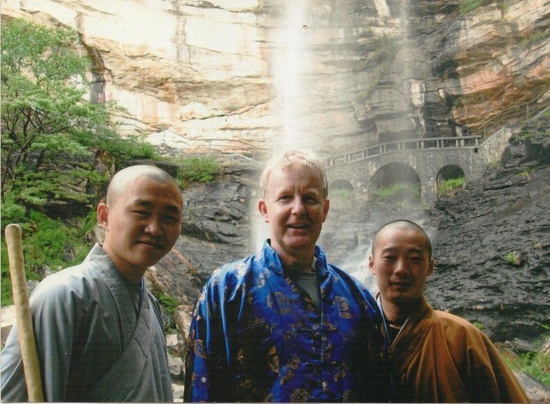 Three men are posing for a picture in front of a waterfall.