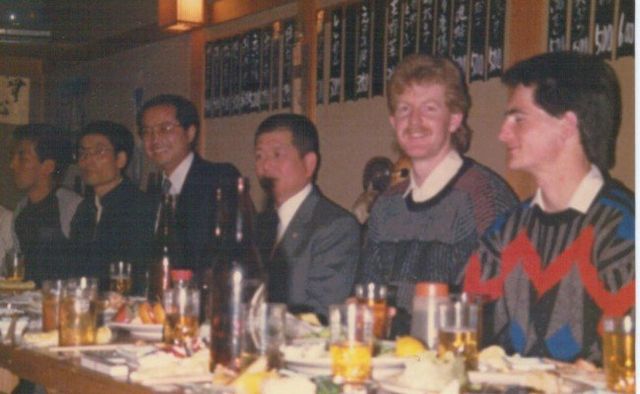 A group of men are sitting at a table with drinks and food