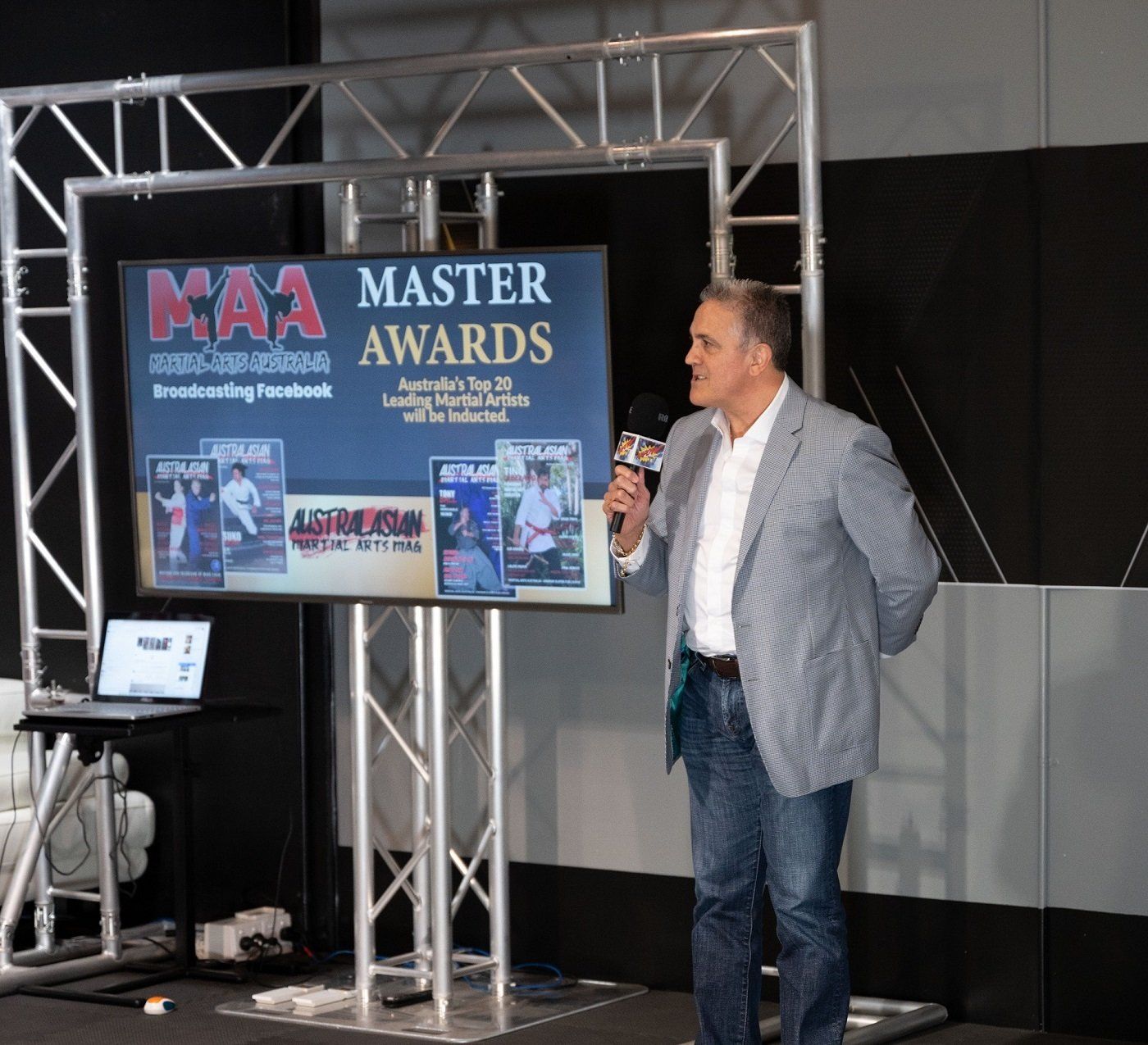 A man stands in front of a screen that says master awards