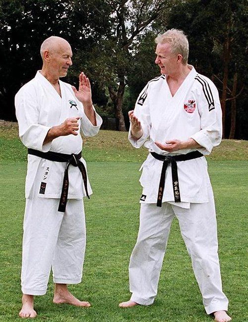 Two men in karate uniforms are standing in a grassy field