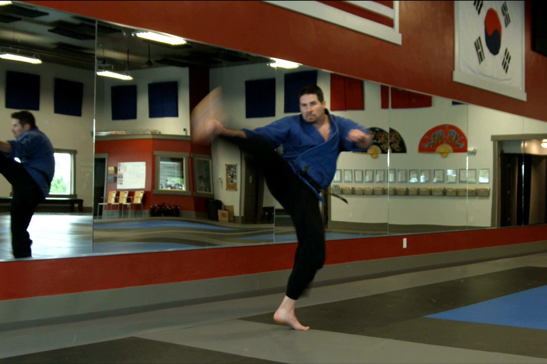 A man is kicking in front of a mirror in a gym