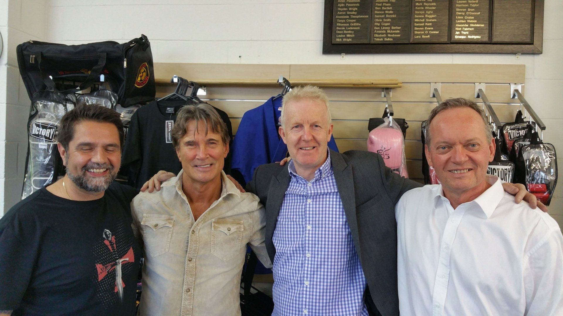 Four men are posing for a picture in front of a clothing rack