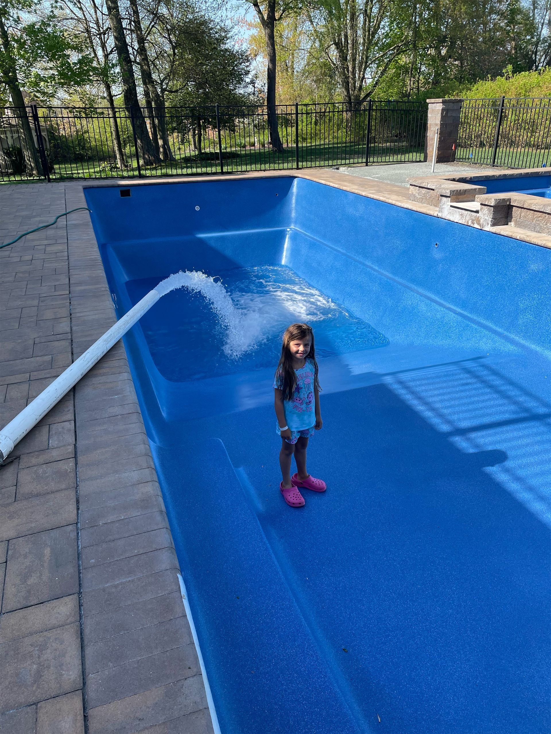 A little girl is standing next to a swimming pool