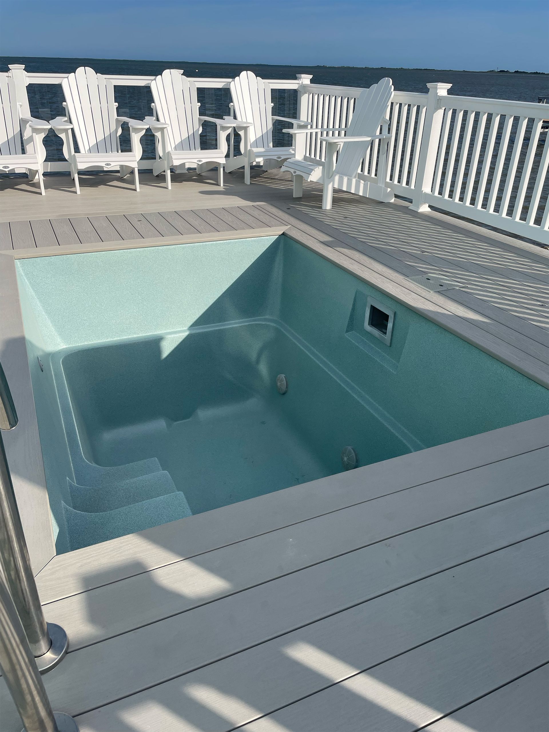 A large swimming pool on a deck with chairs in the background