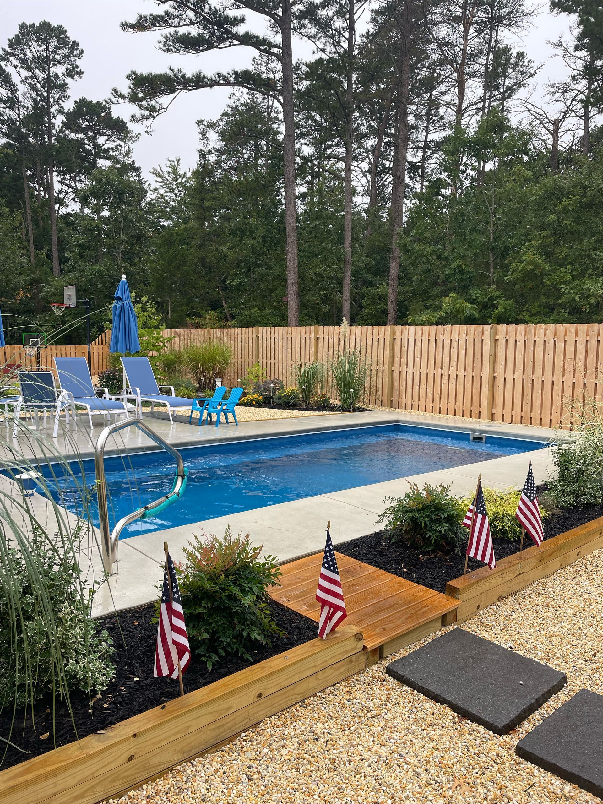 A large swimming pool is surrounded by a wooden fence and chairs.