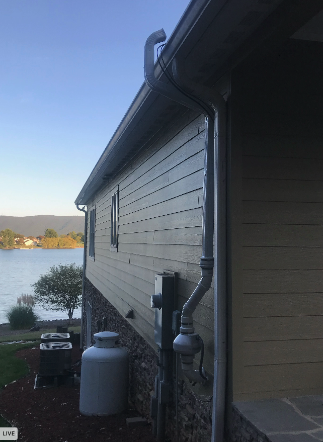 The side of a house with a gutter and a propane tank