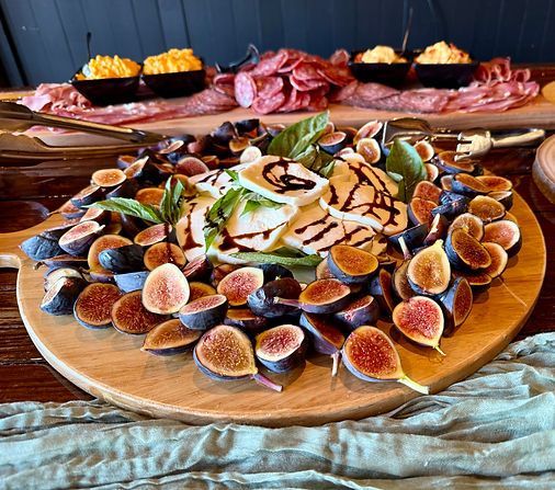 Assorted figs and charcuterie arranged on a wooden serving board with small bowls in the background