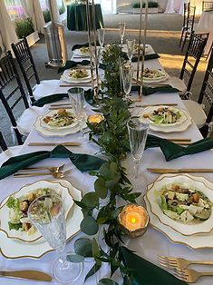 Elegant dining table set with white plates, green napkins, candles, and floral centerpieces