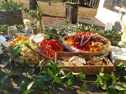 Outdoor buffet table with trays of fresh fruit and vegetables, wrapped in green leaves on a sunny patio