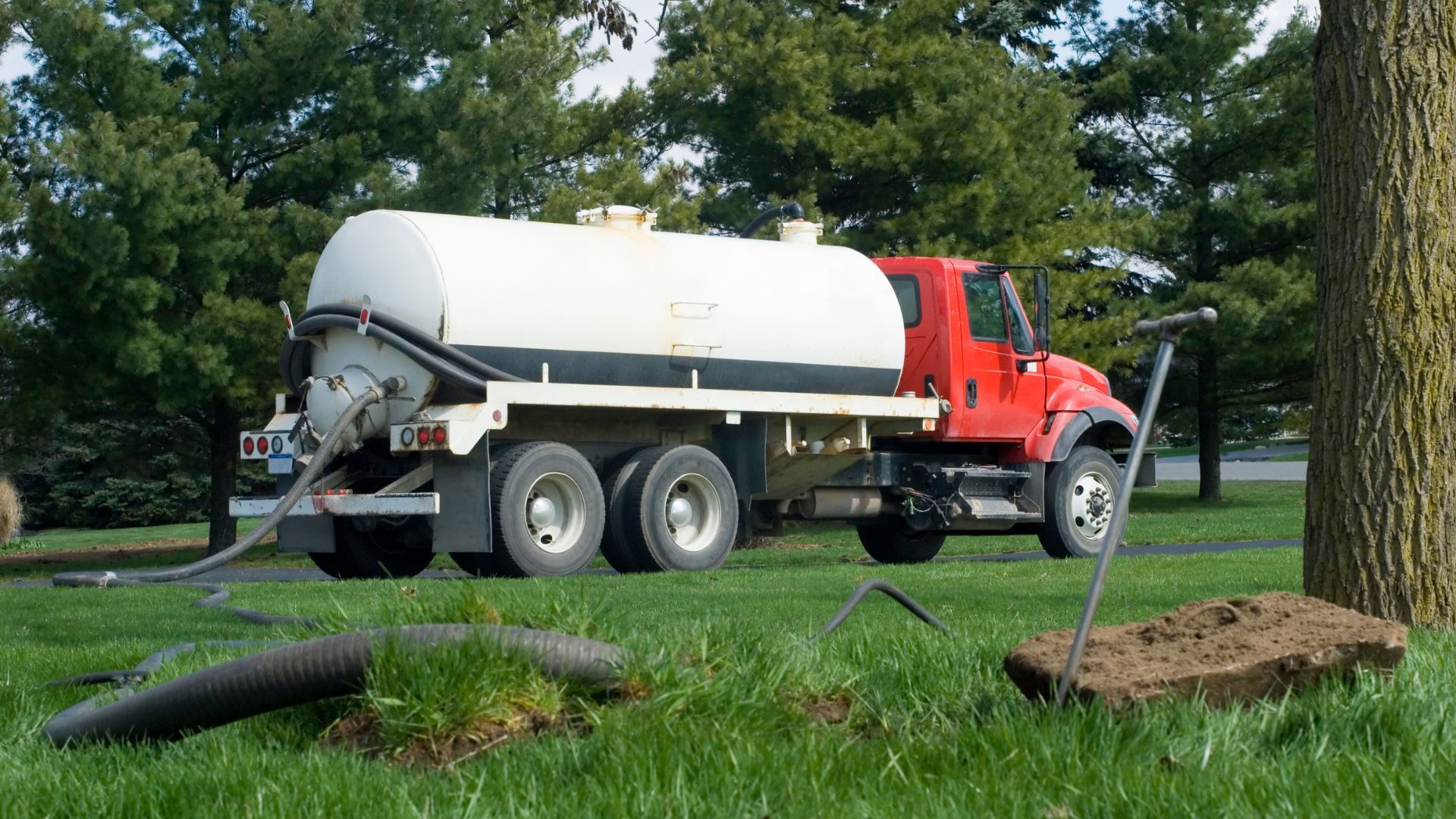 a red and white septic tank truck is driving through a grassy field .