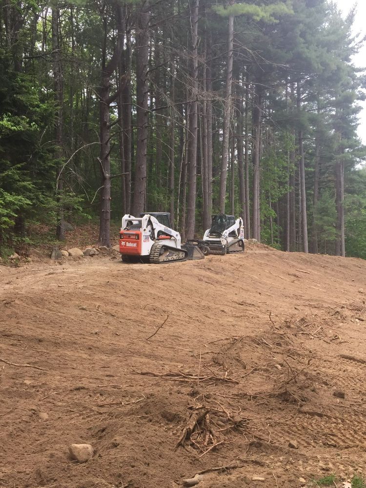 Two bulldozers are sitting in a dirt field in the middle of a forest.
