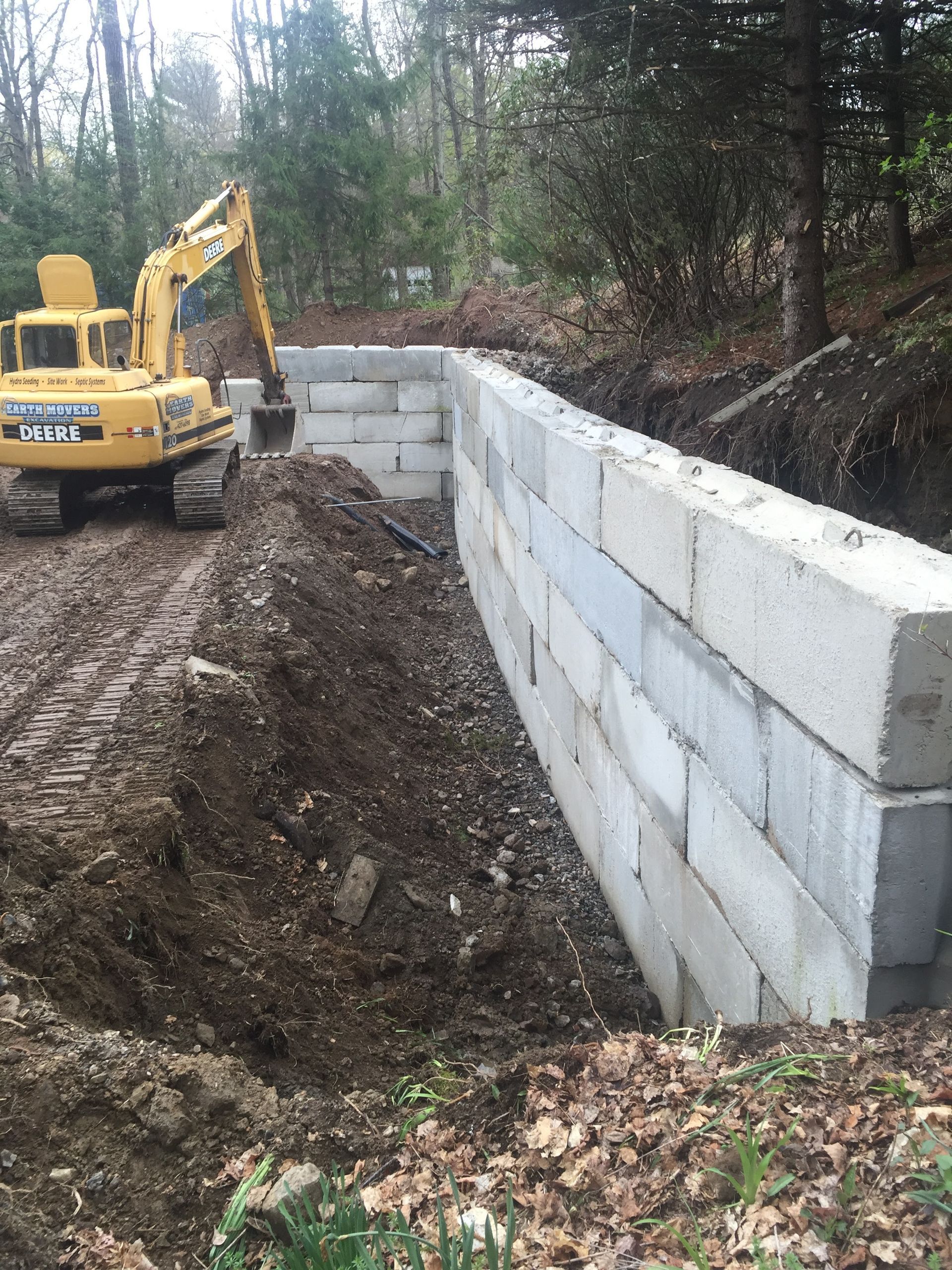A yellow excavator is working on a wall in the woods