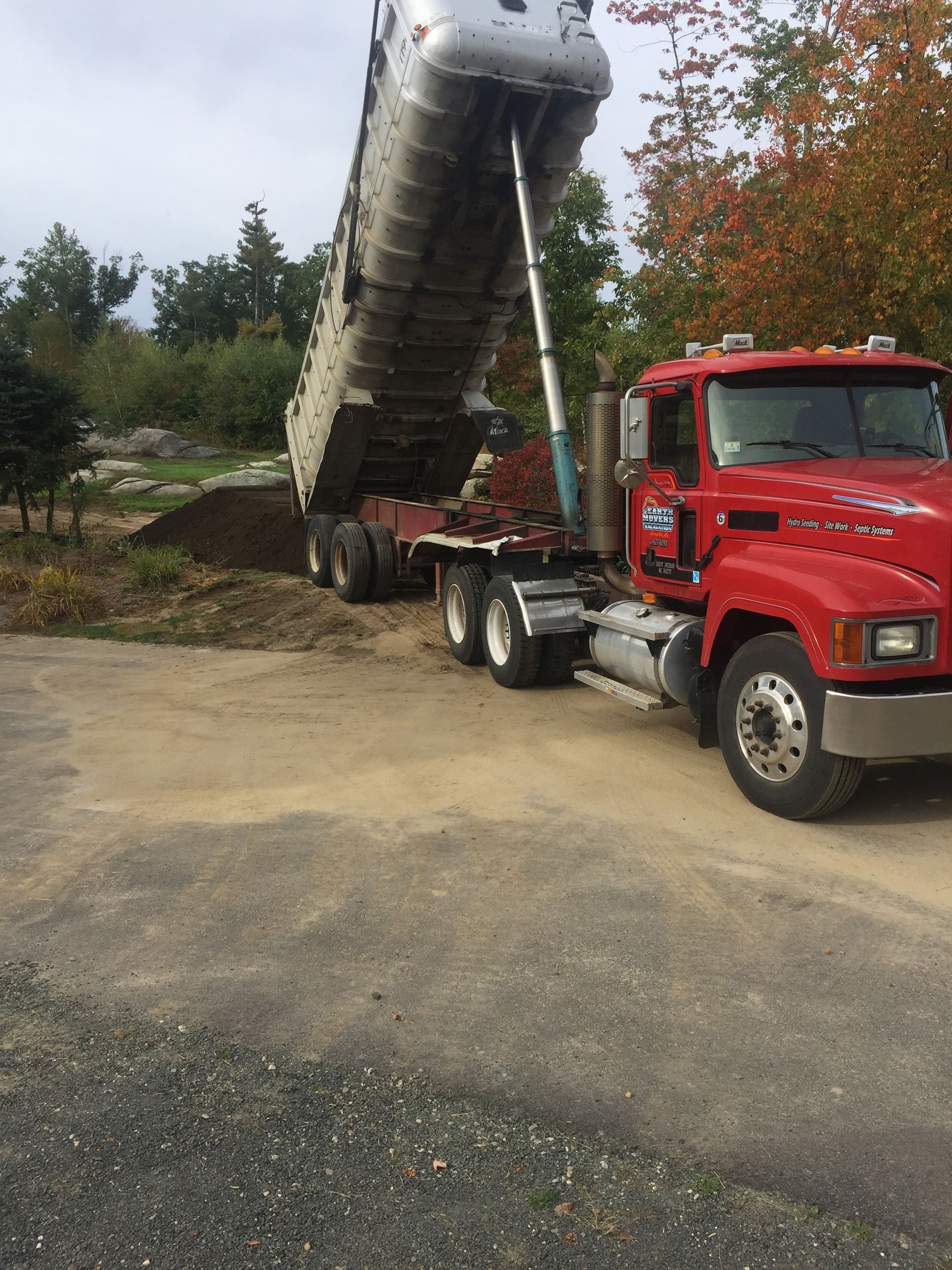 A red dump truck is loading dirt into a trailer.