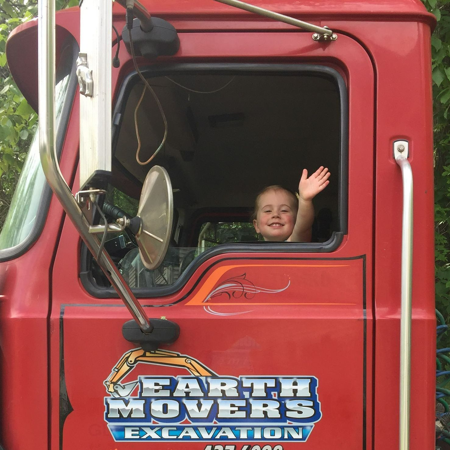 baby sitting in the driver 's seat of a red earth movers excavation truck
