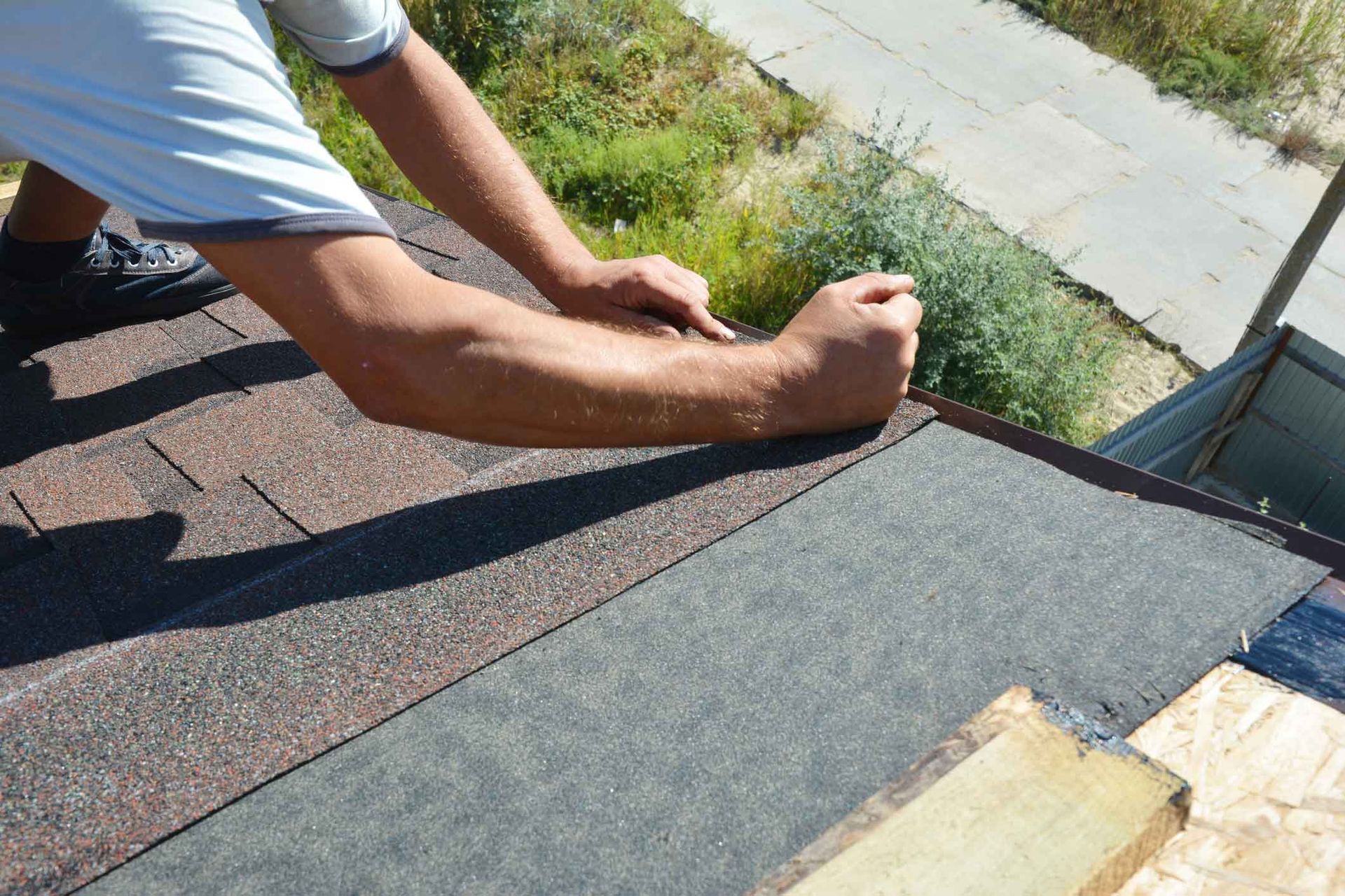 Person installing roof shingles beside a gray ridge cap on a sloped roof