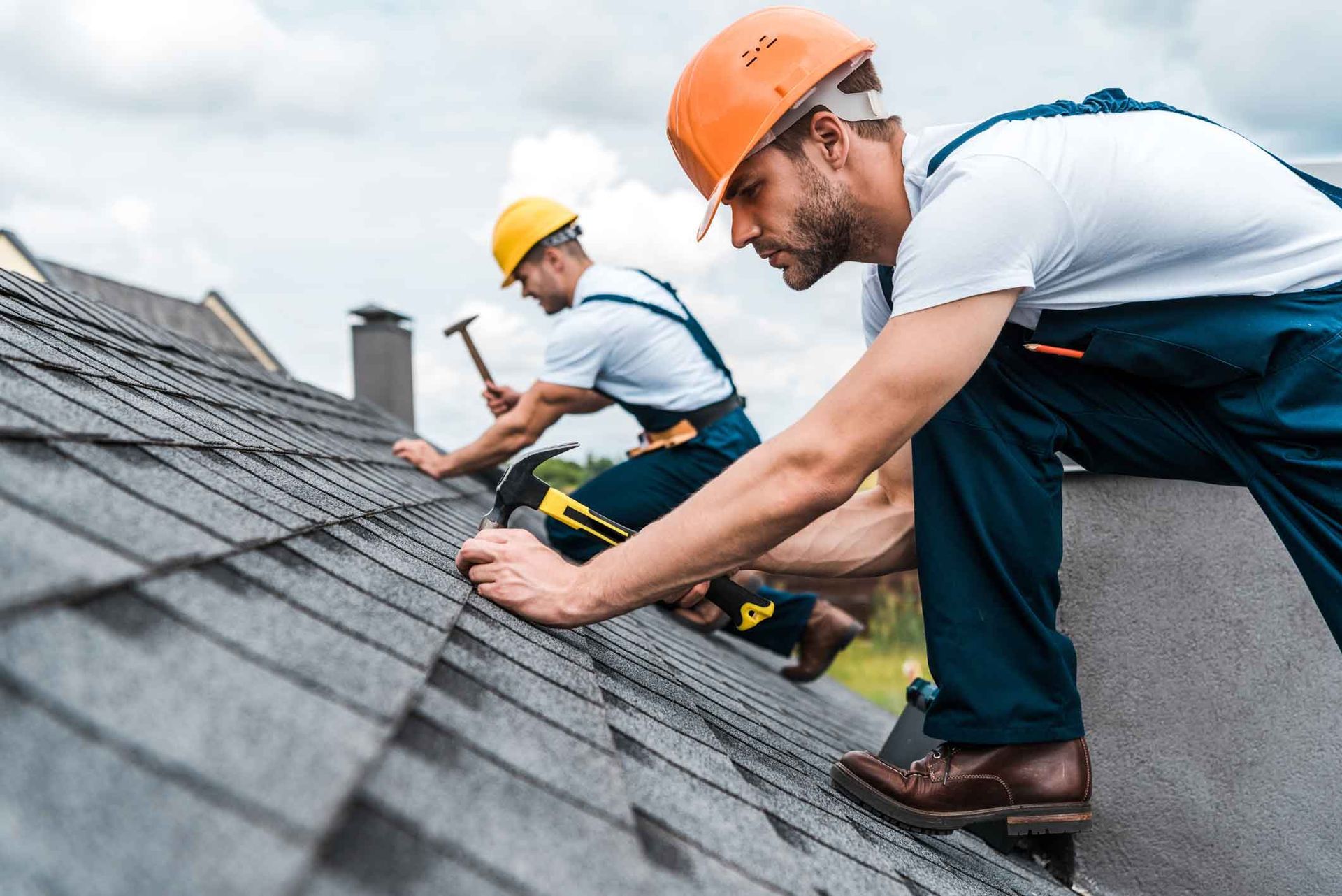Roofers installing asphalt shingles on a residential roof using hammers and safety gear. Roofers installing asphalt shingles on a residential roof using hammers and safety gear.