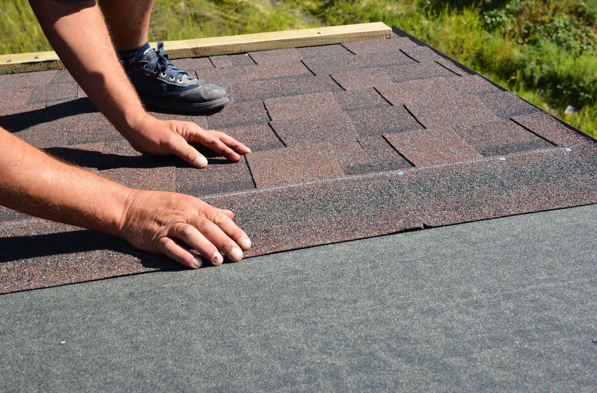 Hands aligning and installing asphalt roofing shingles on a residential roof. Hands aligning and installing asphalt roofing shingles on a residential roof.
