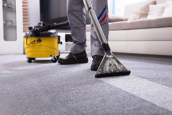 A person is using a vacuum cleaner to clean a carpet in a living room.