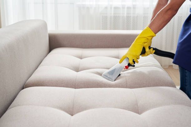 A person is cleaning a couch with a vacuum cleaner.