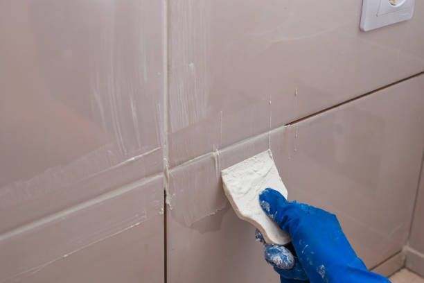 A person is cleaning a tile wall with a spatula.